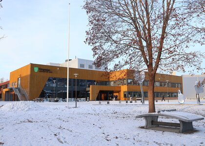 Bilde av forsiden av skolebygget på en vinterdag. Det ligger ett tynt lag med snø på bakken og vi kan se noen elever på vei ut av bygget. - Klikk for stort bilde