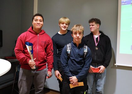 Fire gutter poserer og smiler. De holder gavekort, en har medalje rundt halsen og en holder på en pokal.